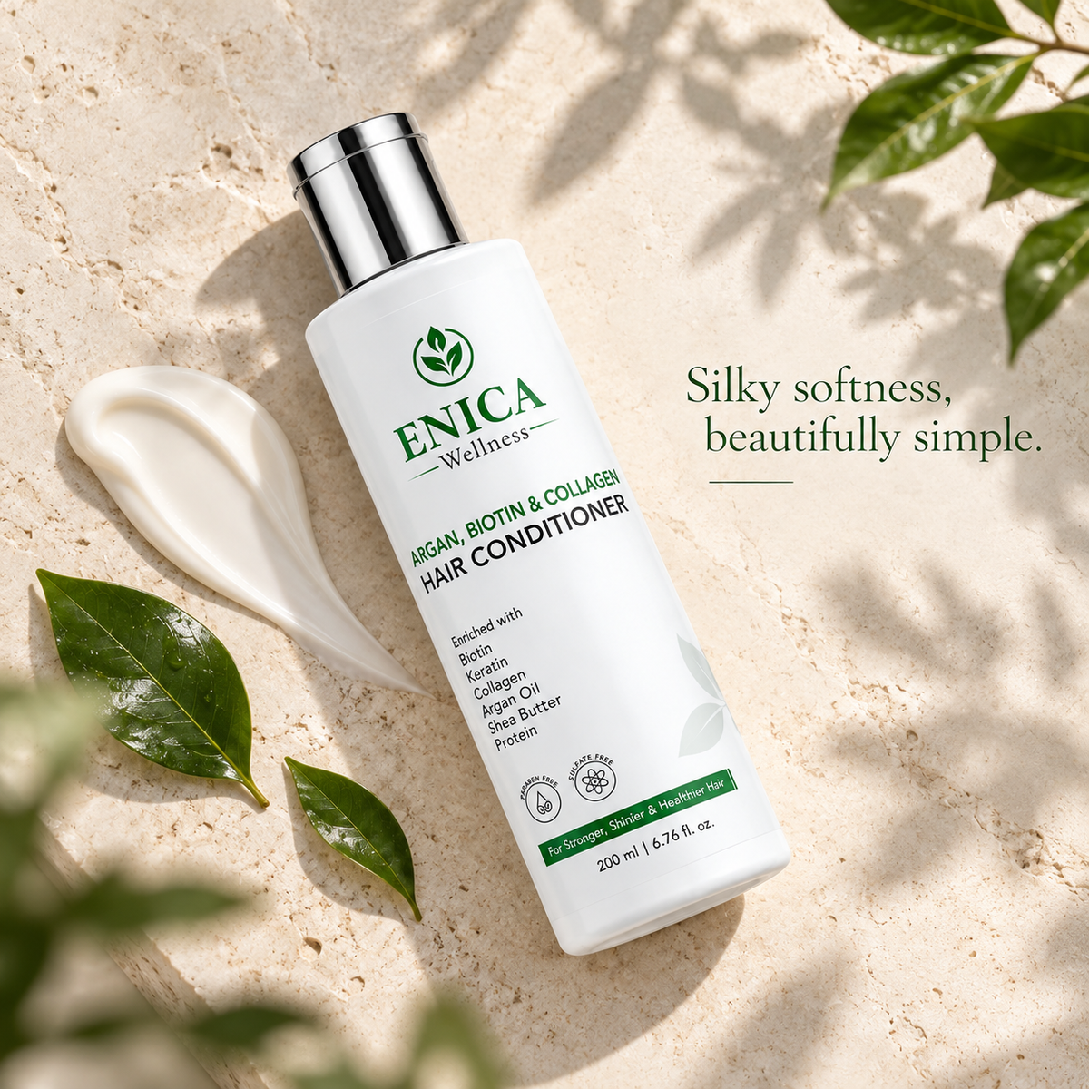 A bottle of ENICA Wellness Argan, Biotin & Collagen Hair Conditioner lies on a textured beige stone surface, styled with a dollop of white conditioner, green leaves, and soft shadows. Text on the right reads 'Silky softness, beautifully simple.