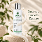 A bottle of ENICA Wellness Argan, Biotin & Collagen Hair Conditioner is displayed on a stone pedestal with a decorative swirl of cream and floating droplets, set against a soft-focus background of green leaves and beige tones.